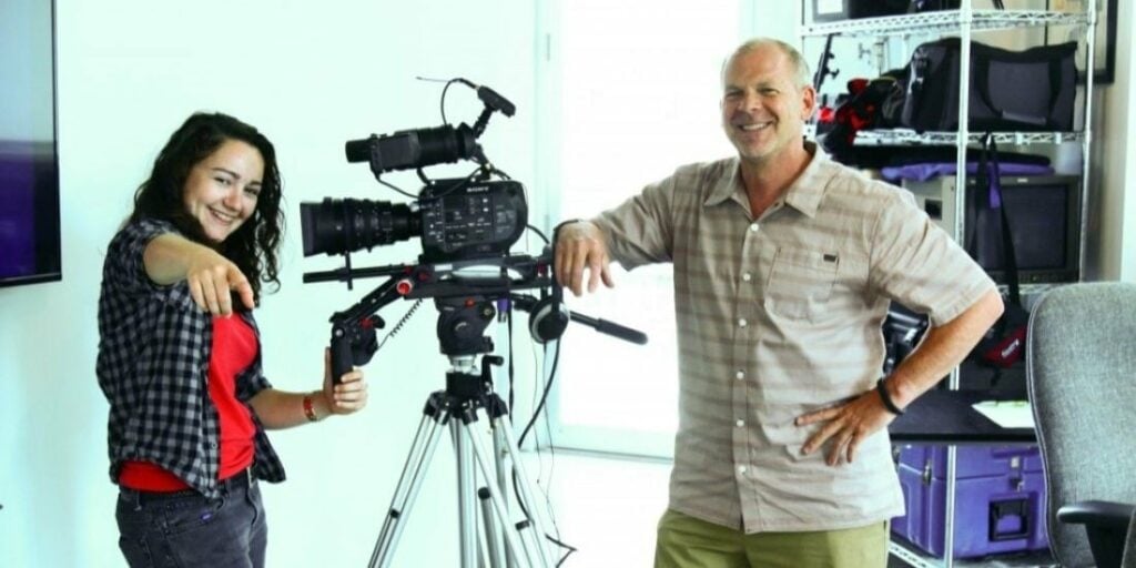 Film producer and Film Connection mentor and female student with camera in production company to help illustrate careers in cinematography.